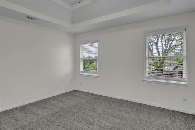 empty room with visible vents, a raised ceiling, baseboards, and dark carpet