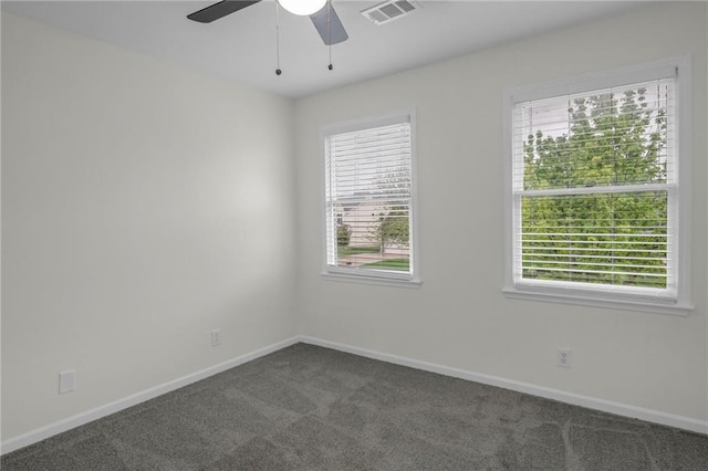 spare room with a wealth of natural light, dark carpet, and visible vents