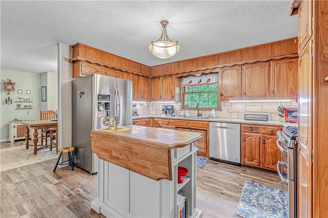 8739 Lafayette Ave, Kansas City, KS 66109 - kitchen featuring appliances with stainless steel finishes, a sink, light wood-style flooring, a textured ceiling, and brown cabinets