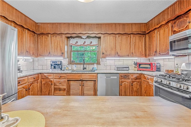 8739 Lafayette Ave, Kansas City, KS 66109 - kitchen with appliances with stainless steel finishes, a sink, a textured ceiling, backsplash, and brown cabinets