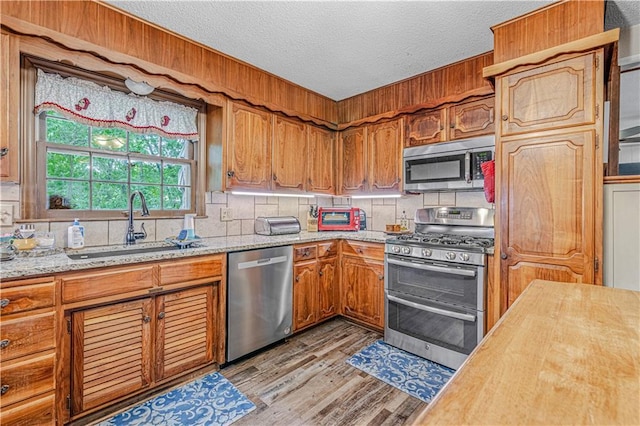 8739 Lafayette Ave, Kansas City, KS 66109 - kitchen with appliances with stainless steel finishes, light wood-style floors, tasteful backsplash, a textured ceiling, and a sink
