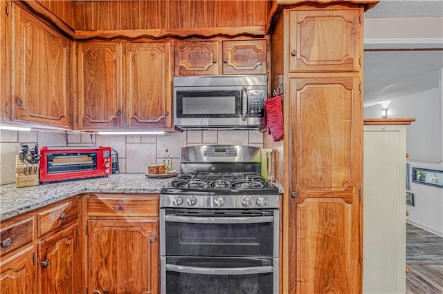 8739 Lafayette Ave, Kansas City, KS 66109 - kitchen featuring appliances with stainless steel finishes, backsplash, and brown cabinetry