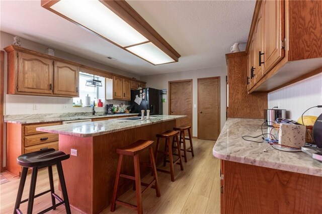 403 S 2nd St, Drexel, MO 64742 - kitchen with brown cabinets, freestanding refrigerator, a breakfast bar area, light wood finished floors, and a kitchen island