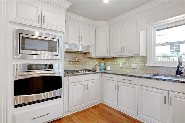 9000 W 104th St, Overland Park, KS 66212 - kitchen featuring under cabinet range hood, white cabinets, a sink, appliances with stainless steel finishes, and backsplash