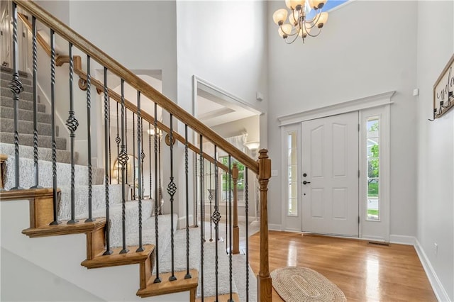 entrance foyer with a high ceiling, a chandelier, stairs, baseboards, and wood finished floors