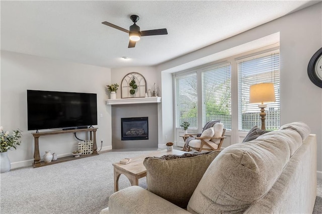 living room with a tiled fireplace, baseboards, ceiling fan, and carpet floors