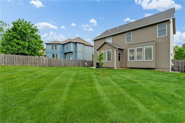 rear view of property featuring fence, a shingled roof, and a yard