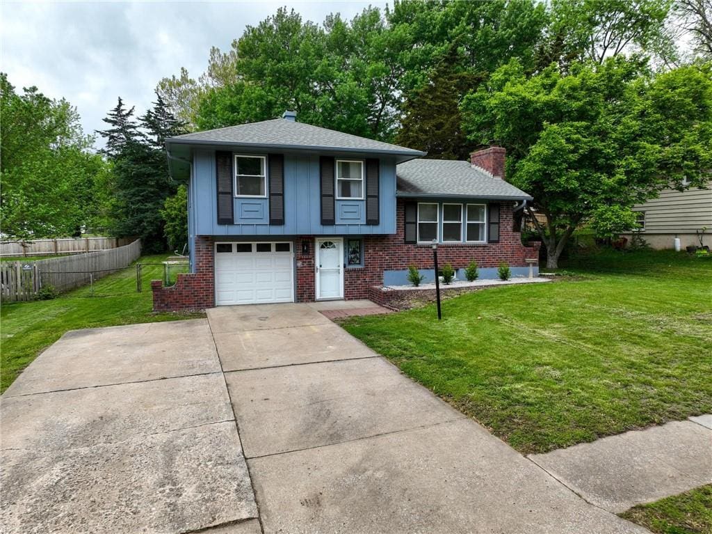tri-level home with fence, an attached garage, a front lawn, brick siding, and driveway