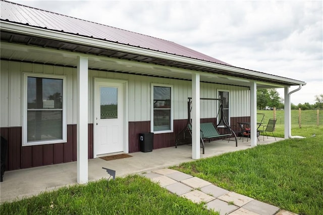rear view of property with board and batten siding, a yard, a patio area, and metal roof