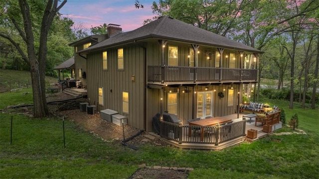 606 W Red Bridge Rd, Kansas City, MO 64114 - back of property at dusk with board and batten siding, an outdoor hangout area, a chimney, a yard, and a wooden deck