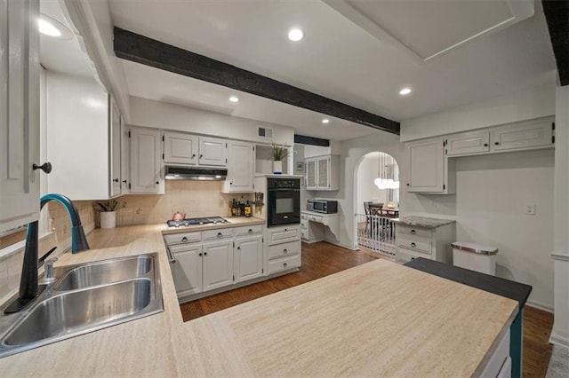606 W Red Bridge Rd, Kansas City, MO 64114 - kitchen featuring black oven, stainless steel microwave, beamed ceiling, decorative backsplash, and under cabinet range hood