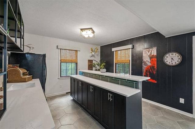 606 W Red Bridge Rd, Kansas City, MO 64114 - kitchen featuring dark cabinets, a center island, light countertops, light tile patterned floors, and freestanding refrigerator
