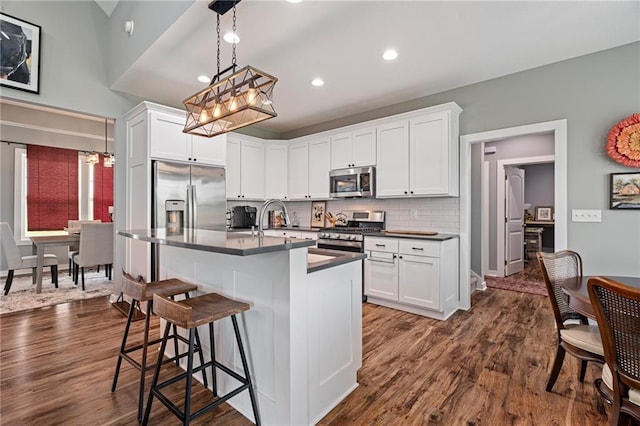 kitchen with dark countertops, stainless steel appliances, dark wood finished floors, and a kitchen bar