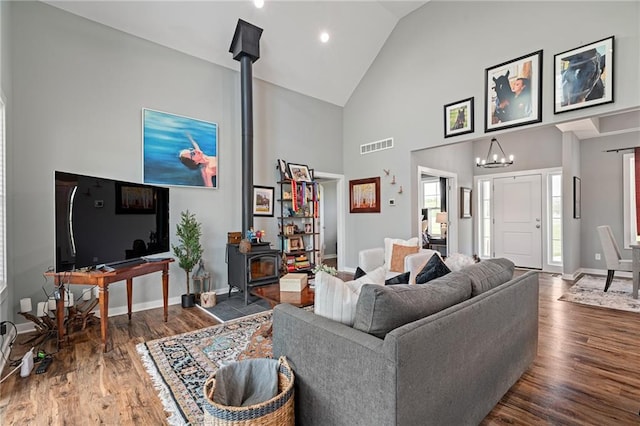 living area with a wood stove, high vaulted ceiling, baseboards, wood finished floors, and visible vents