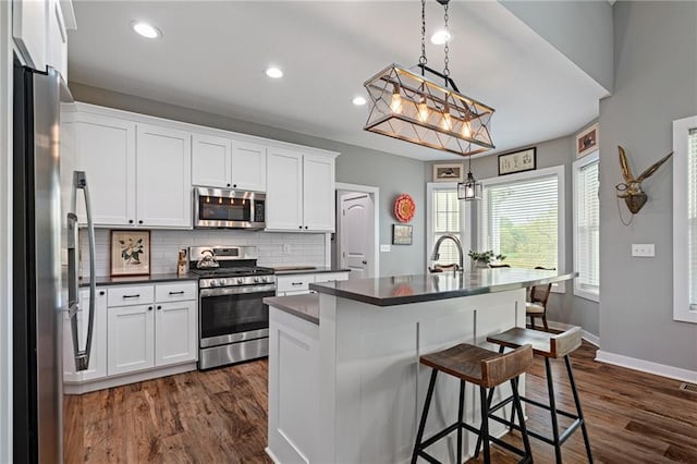 kitchen featuring decorative backsplash, dark countertops, stainless steel appliances, white cabinetry, and dark wood-type flooring
