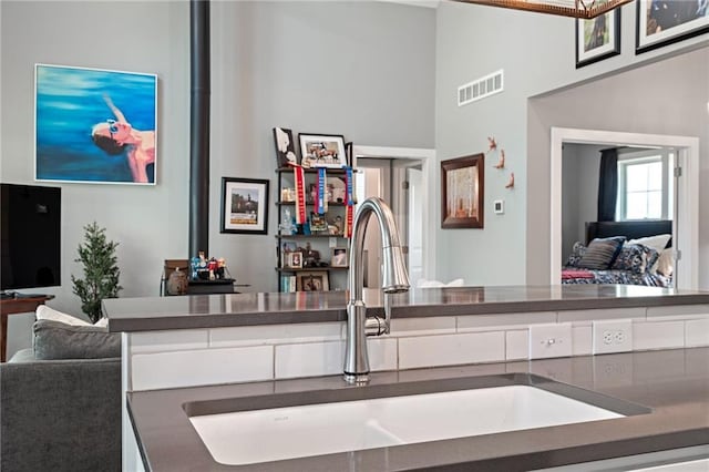 kitchen featuring a towering ceiling, visible vents, dark countertops, a sink, and open floor plan