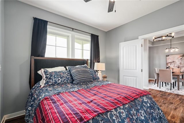bedroom featuring baseboards, ceiling fan with notable chandelier, and wood finished floors