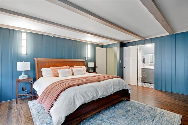 bedroom featuring beam ceiling, wood finished floors, and connected bathroom