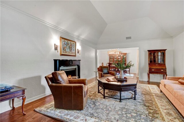 living area featuring vaulted ceiling, a lit fireplace, wood finished floors, a chandelier, and baseboards