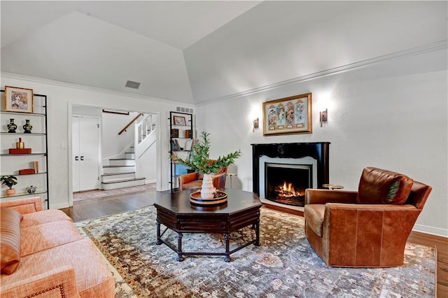 living area with lofted ceiling, wood finished floors, a warm lit fireplace, stairs, and baseboards
