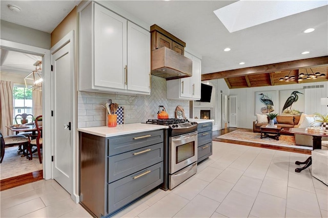 kitchen featuring stainless steel gas range, gray cabinets, a skylight, light countertops, and tasteful backsplash