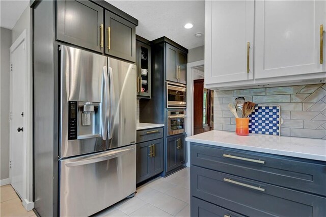 kitchen with stainless steel appliances, backsplash, light tile patterned flooring, and glass insert cabinets