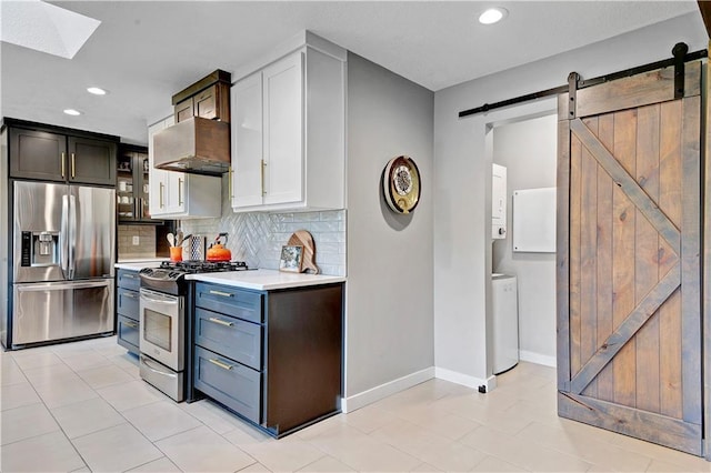 kitchen featuring stainless steel appliances, exhaust hood, light countertops, a barn door, and washer and clothes dryer