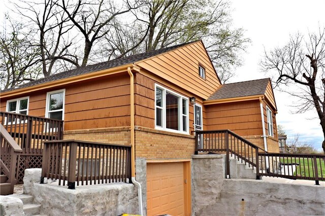 3417 Jackson Ave, Kansas City, MO 64128 - view of side of property featuring roof with shingles, an attached garage, stairway, and brick siding