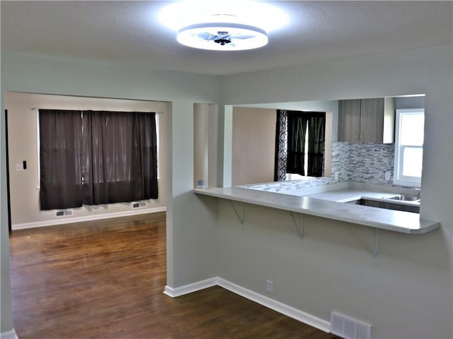 3417 Jackson Ave, Kansas City, MO 64128 - kitchen with dark wood-style flooring, a breakfast bar area, light countertops, backsplash, and visible vents