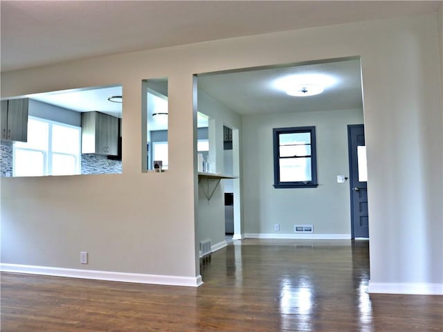 3417 Jackson Ave, Kansas City, MO 64128 - unfurnished living room featuring visible vents, baseboards, plenty of natural light, and dark wood-style floors