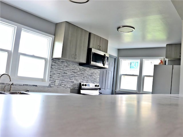 3417 Jackson Ave, Kansas City, MO 64128 - kitchen featuring appliances with stainless steel finishes, a sink, light countertops, a healthy amount of sunlight, and tasteful backsplash