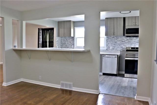 3417 Jackson Ave, Kansas City, MO 64128 - kitchen with a breakfast bar area, backsplash, visible vents, appliances with stainless steel finishes, and dark wood-style floors