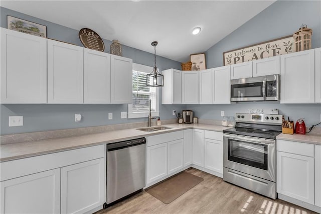 kitchen featuring light countertops, white cabinets, a sink, appliances with stainless steel finishes, and vaulted ceiling