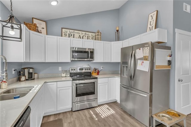 kitchen featuring appliances with stainless steel finishes, a sink, light countertops, white cabinetry, and light wood-type flooring