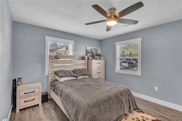 bedroom with a textured ceiling, baseboards, ceiling fan, and wood finished floors