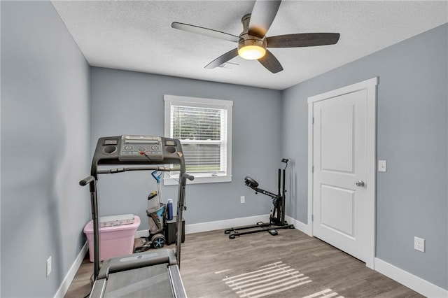workout area featuring baseboards, a textured ceiling, ceiling fan, and wood finished floors