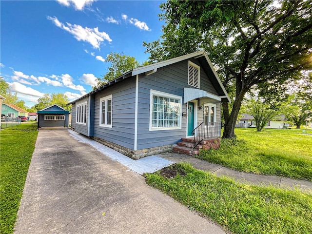 bungalow-style house with concrete driveway, an outbuilding, and a front yard