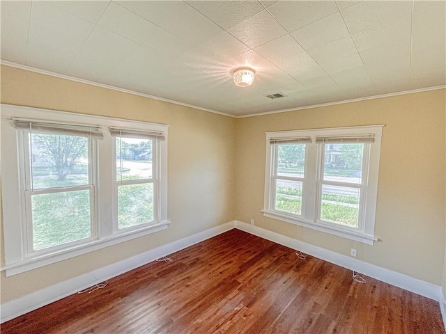 empty room featuring crown molding, dark wood finished floors, plenty of natural light, and visible vents