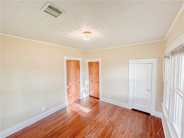 unfurnished bedroom featuring crown molding, baseboards, visible vents, and wood finished floors