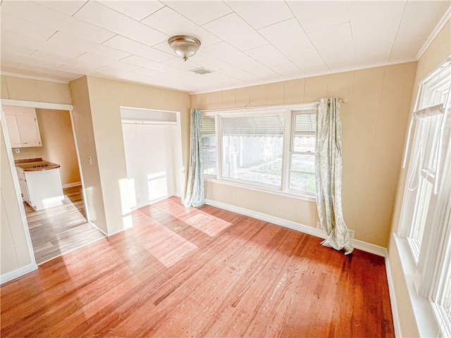 unfurnished bedroom featuring baseboards, ornamental molding, light wood-style flooring, and a closet
