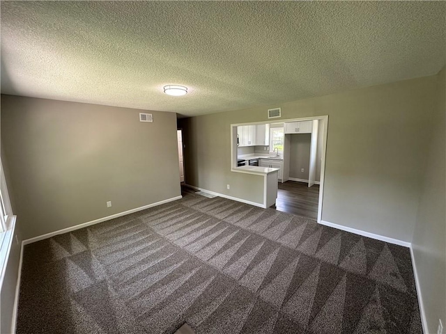 empty room featuring visible vents, a sink, baseboards, and dark colored carpet