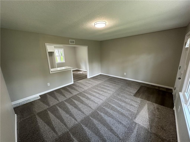 unfurnished bedroom featuring baseboards, dark colored carpet, a textured ceiling, and visible vents