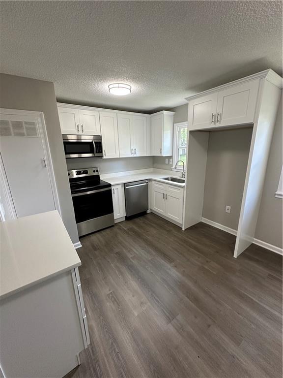 kitchen featuring appliances with stainless steel finishes, a sink, light countertops, white cabinetry, and dark wood-style floors