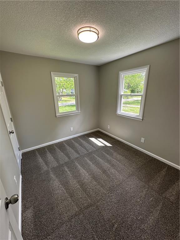 empty room featuring dark colored carpet, a textured ceiling, and a wealth of natural light