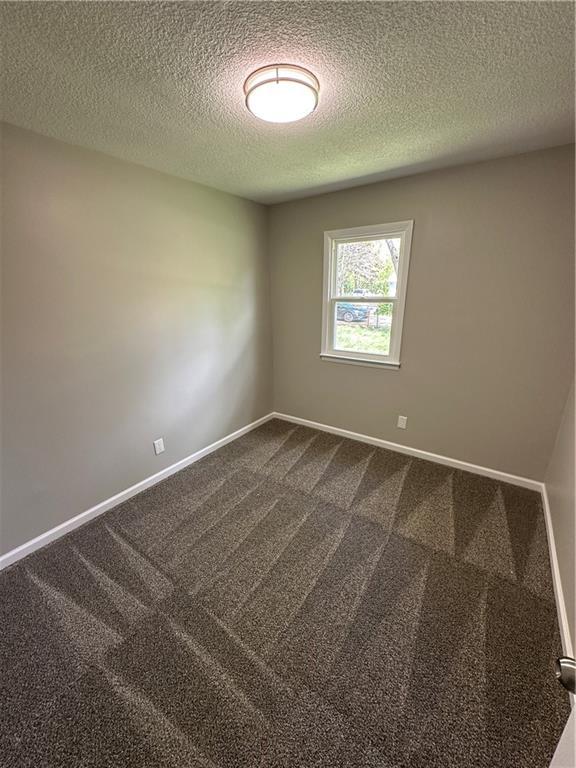 spare room with dark carpet, a textured ceiling, and baseboards