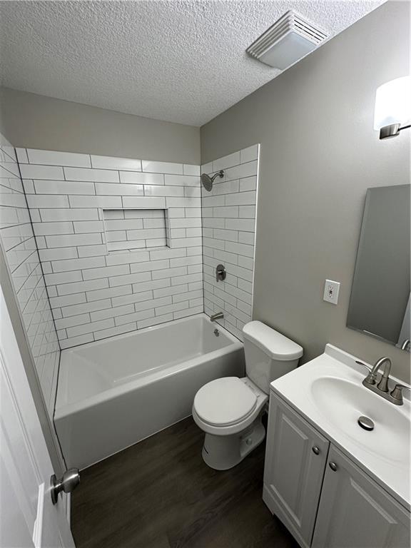 bathroom with visible vents, wood finished floors, bathing tub / shower combination, toilet, and a textured ceiling