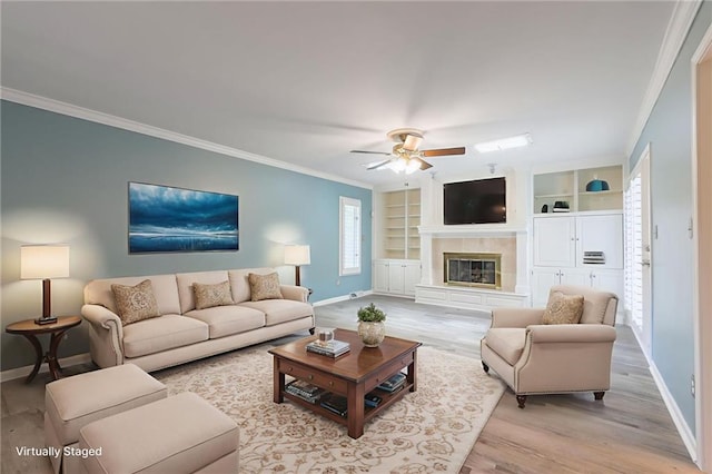 11801 Avila Dr, Kansas City, MO 64114 - living room featuring light wood-style flooring, ornamental molding, a ceiling fan, a glass covered fireplace, and built in shelves