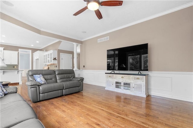 7406 W 145th Ter, Overland Park, KS 66223 - living area featuring a ceiling fan, light wood-type flooring, a wainscoted wall, ornate columns, and ornamental molding