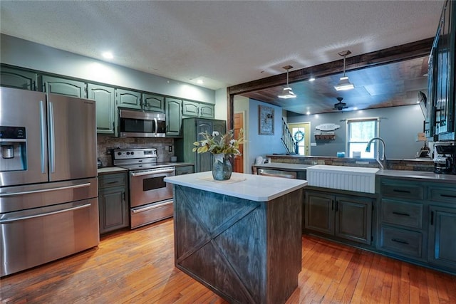 kitchen featuring appliances with stainless steel finishes, light wood-style flooring, backsplash, pendant lighting, and a kitchen island