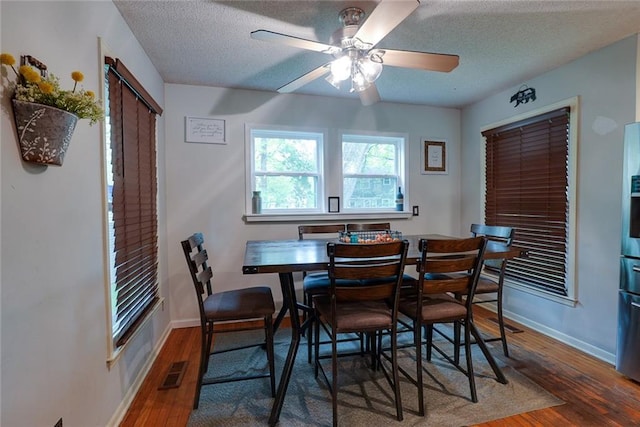 dining space with visible vents, baseboards, a textured ceiling, and wood finished floors